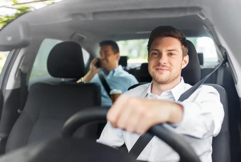 A driver and front passenger seated in a car, both wearing fastened three-point seat belts.
