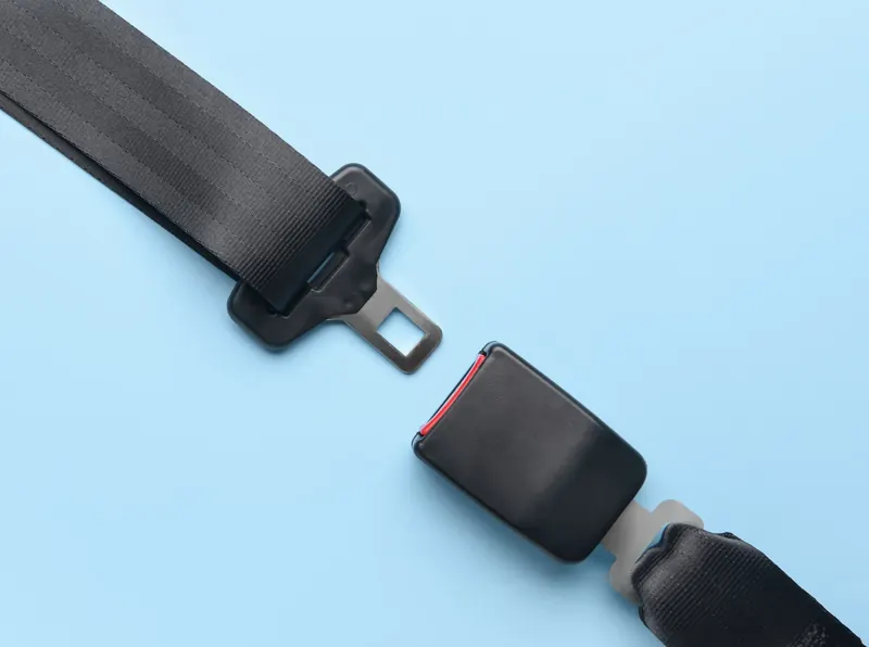 A seat belt laid flat on a pale background, showing the webbing and latch plate separated from the buckle receiver on its own webbing stalk.